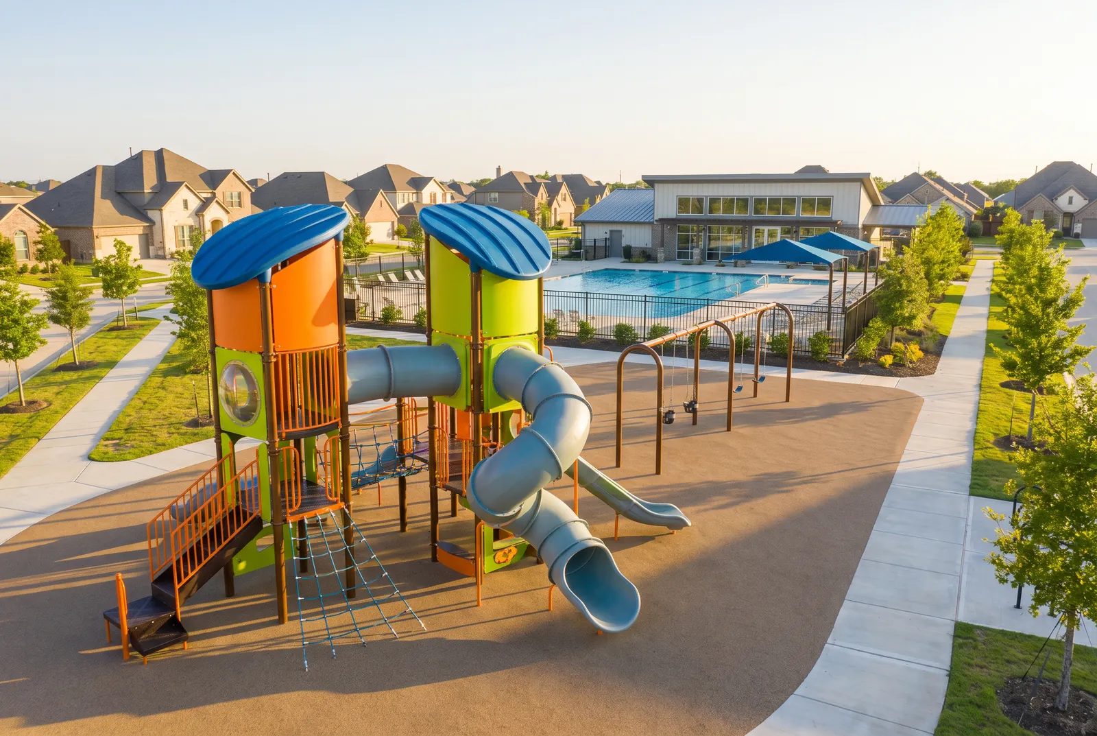 A subdivision amenity playground with orange and lime-green towers, blue roofs and tube slides beside the community pool