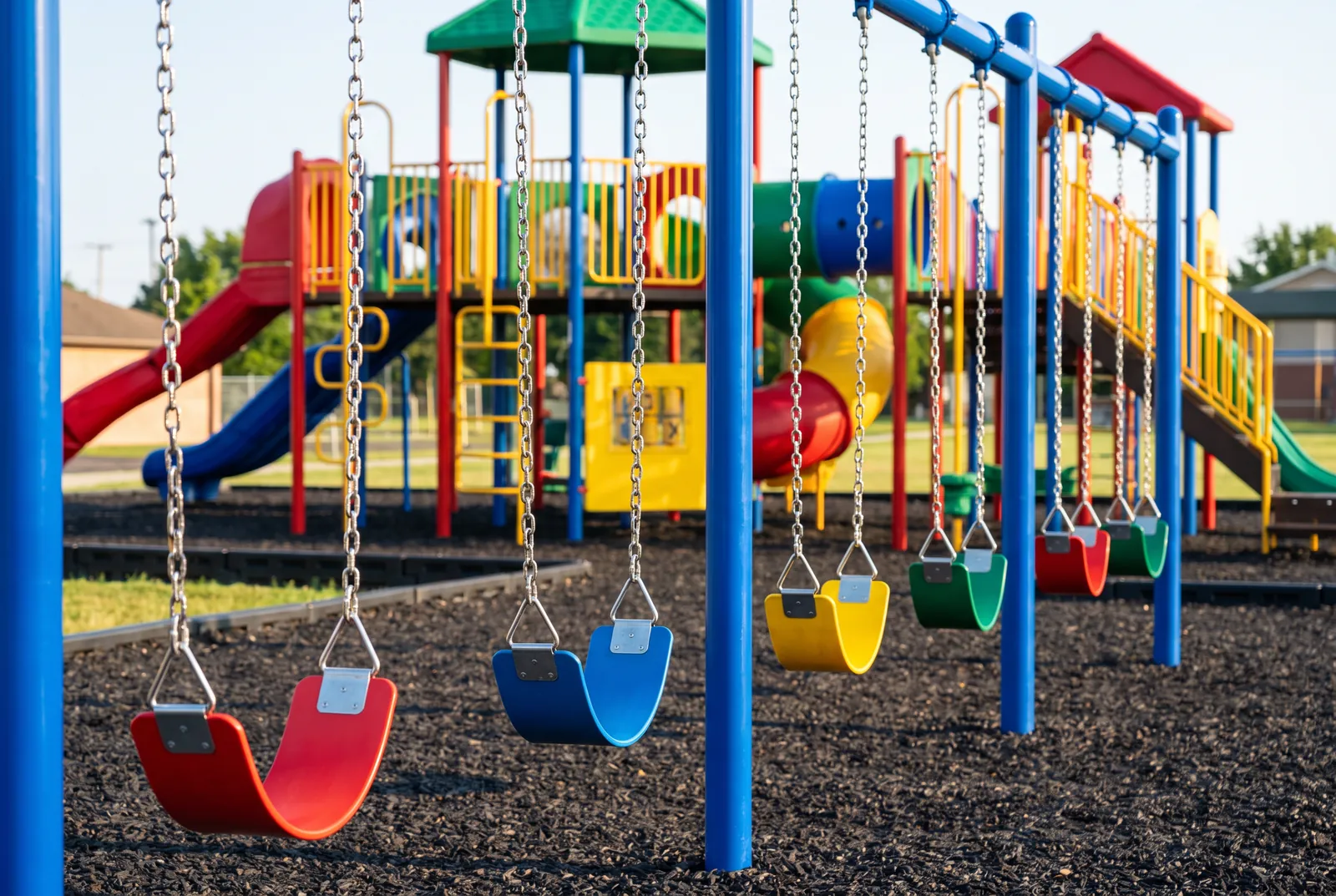 A swing bay with brand-new chains and red, blue, yellow and green seats on a freshly painted blue frame over new rubber mulch