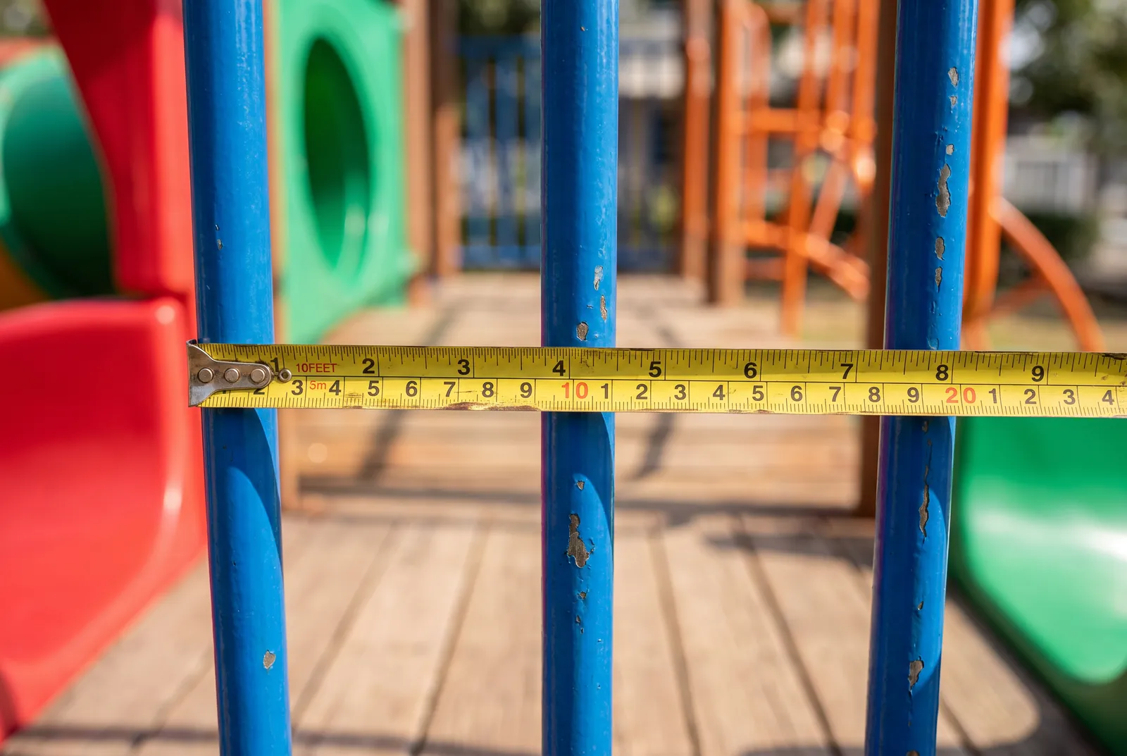 A tape measure stretched across the opening between the bars of a blue playground guardrail
